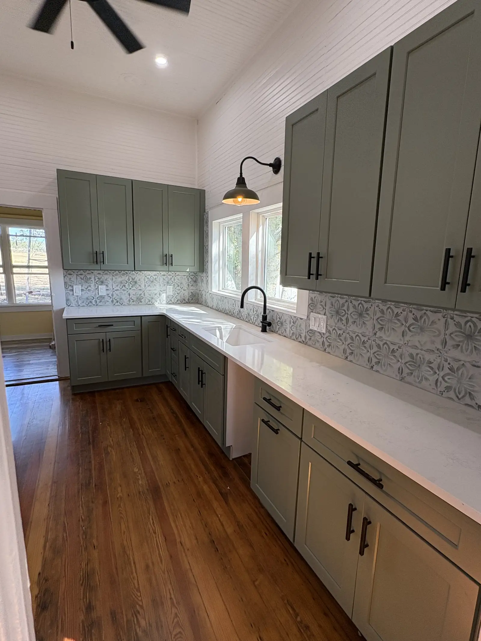 Restored farmhouse kitchen with sage green cabinets and open wood shelving